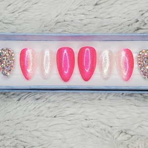 Peut inclure: Un ensemble de dix faux ongles press-on en d&eacute;grad&eacute; de rose et de blanc avec des paillettes et des strass.