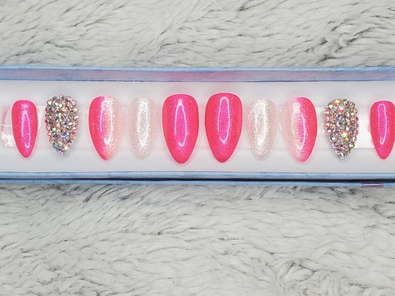 Peut inclure: Un ensemble de dix faux ongles press-on en d&eacute;grad&eacute; de rose et de blanc avec des paillettes et des strass.