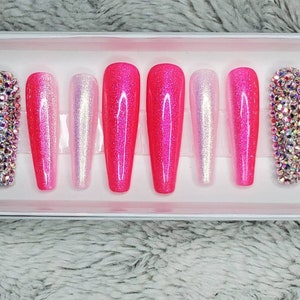 Peut inclure: Un ensemble de dix faux ongles press-on en d&eacute;grad&eacute; de rose et de blanc avec des strass. Les ongles sont longs et ont une forme de cercueil.