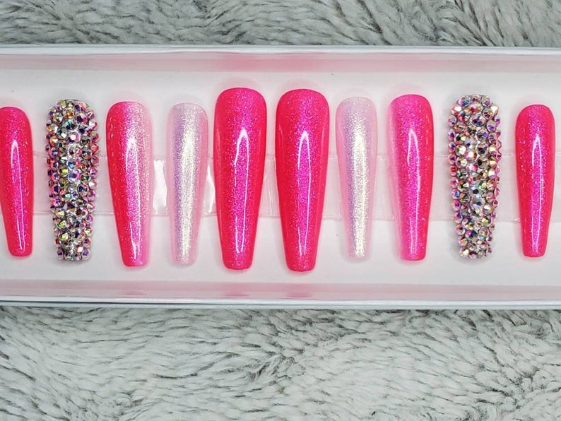 Peut inclure: Un ensemble de dix faux ongles press-on en d&eacute;grad&eacute; de rose et de blanc avec des strass. Les ongles sont longs et ont une forme de cercueil.
