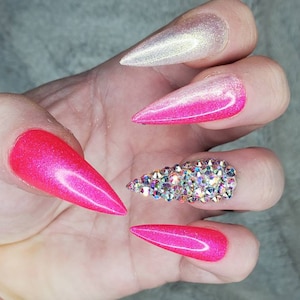 Peut inclure: Gros plan d'une main avec de longs ongles en stiletto ombr&eacute;s rose et blanc. Un ongle est orn&eacute; d'un groupe de strass transparents.