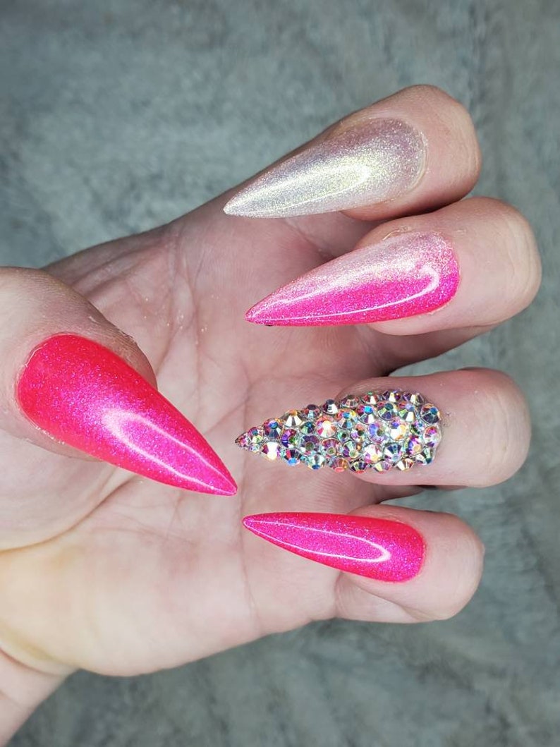 Peut inclure: Gros plan d'une main avec de longs ongles en stiletto ombr&eacute;s rose et blanc. Un ongle est orn&eacute; d'un groupe de strass transparents.