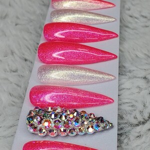 Peut inclure: Ensemble de dix faux ongles &agrave; presser de couleur d&eacute;grad&eacute;e rose et blanche avec des paillettes. Un ongle pr&eacute;sente un grand groupe de strass iris&eacute;s.