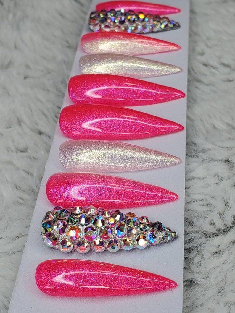 Peut inclure: Ensemble de dix faux ongles &agrave; presser de couleur d&eacute;grad&eacute;e rose et blanche avec des paillettes. Un ongle pr&eacute;sente un grand groupe de strass iris&eacute;s.