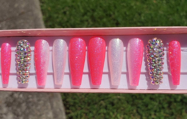 Peut inclure: Un ensemble de dix faux ongles longs, en d&eacute;grad&eacute; de rose et blanc avec des strass sur deux ongles.
