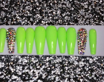 May include: Set of ten lime green press-on nails with a single nail featuring a large, clear rhinestone cluster.