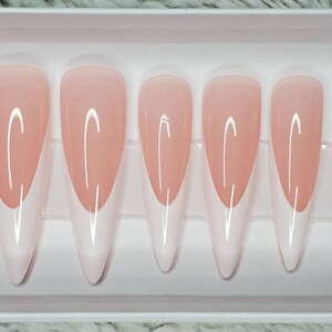 Könnte beinhalten: Set mit zehn langen, mandelförmigen, künstlichen Nägeln mit weißer Spitze und hellrosa Basis.