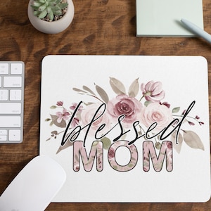 May include: A white mouse mat with a floral design and the text "blessed MOM" in black and pink.