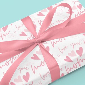 May include: A white gift box with a pink ribbon and a pink and white pattern of hearts and the words "mom" and "I love you".