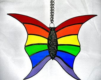 Könnte beinhalten: Ein Buntglas-Schmetterling mit Regenbogenfarben, der an einer silbernen Kette hängt. Der Schmetterling hat ein rotes, orangefarbenes, gelbes, grünes, blaues und violettes Design.