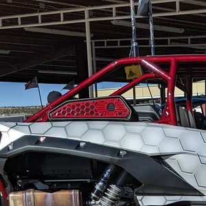 May include: A red and black off-road vehicle with a white honeycomb pattern on the side. The vehicle has a red roll cage and a black exhaust pipe.
