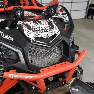 May include: A black and red off-road vehicle with a skull and floral design on the hood. The vehicle has a black metal grille and a red metal bumper with the text "EQUIPMENT POWERED BY TNF".