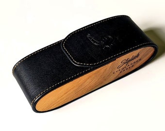 May include: A black leather eyeglasses case with a light brown wooden side panel. The case features a flap closure with white stitching and the text Stylish EYEGLASSES CASES printed in black on the wooden side panel.