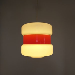 May include: A white and red pendant light with a cylindrical shape. The light has three layers, with the middle layer being red.