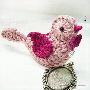 May include: A pink crocheted bird with a pink wing and a silver charm that says "Made with Love".