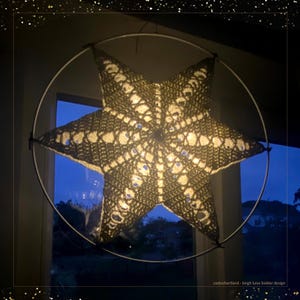 以下が含まれることがあります： 詳細な透かし模様が施された星型の装飾ランプ。 星は円形の金属フレーム内に吊り下げられ、内側から照らされ、夜空の見える窓の前に吊り下げられています。 温かく、魅力的な光源です。