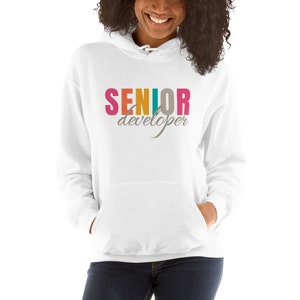 May include: White hooded sweatshirt with a front pocket and a drawstring. The word "SENIOR" is printed across the chest in pink, orange, teal, and grey. Below it, the word "developer" is printed in grey script.