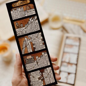May include: A black bookmark with a hand-drawn bookshelf design and the text "100 Classics." The bookmark lists classic literature titles including "Moby Dick," "Hamlet," and "Great Expectations."
