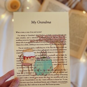 May include: A hand holds a card with a handwritten message about a grandmother. The card features a cartoon illustration of a teacup and a plate of scones. The text on the card reads "My Grandma" and includes a heartfelt message about the author's memories of their grandmother.