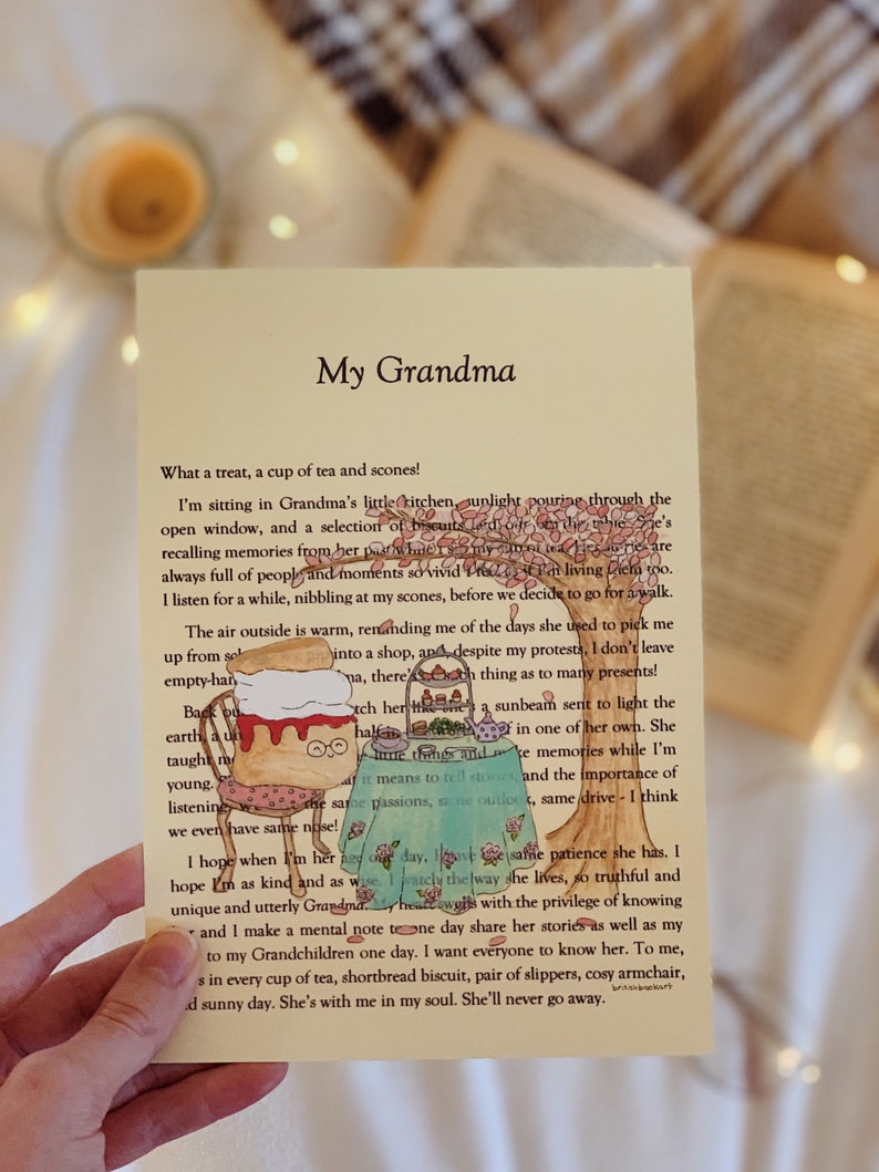 May include: A hand holds a card with a handwritten message about a grandmother. The card features a cartoon illustration of a teacup and a plate of scones. The text on the card reads "My Grandma" and includes a heartfelt message about the author's memories of their grandmother.