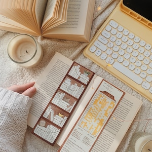 May include: An open book with a bookmark featuring a bookshelf design and the year 2024. A yellow keyboard and a lit candle are also visible. The scene is set on a soft, textured surface.