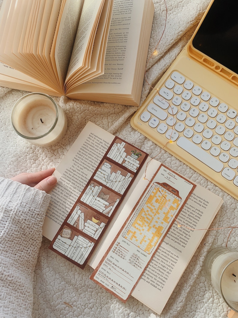 May include: An open book with a bookmark featuring a bookshelf design and the year 2024. A yellow keyboard and a lit candle are also visible. The scene is set on a soft, textured surface.