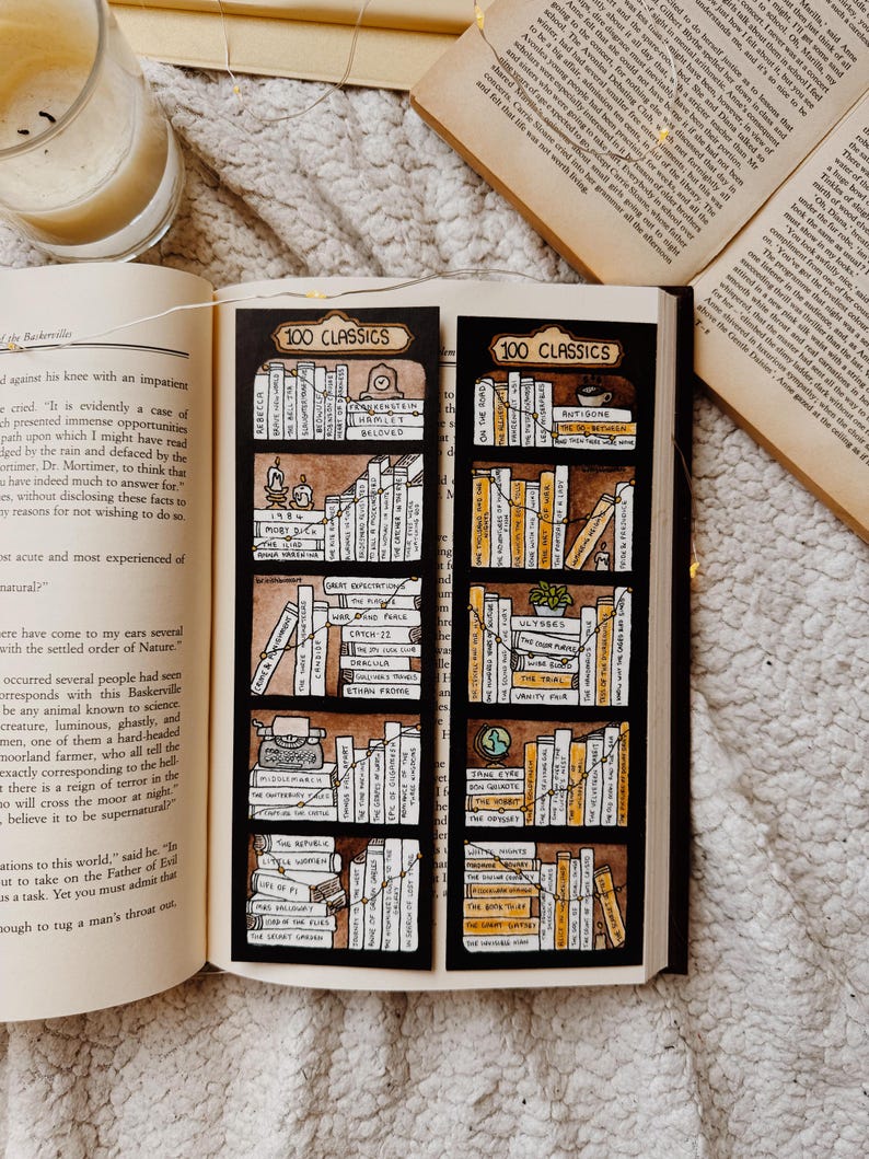 May include: Two black bookmarks, each labelled "100 Classics", display hand-drawn bookshelves filled with classic literature. The bookmarks are placed on an open book, with a lit candle and fairy lights.