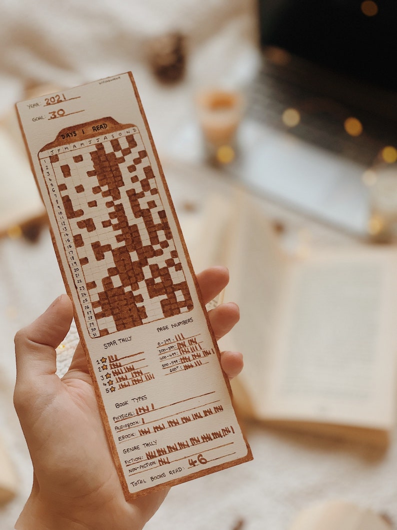 May include: A wooden bookmark with a reading tracker for the year 2021. The bookmark has a grid for tracking days read, star tallies, book types, and genre tallies. The text "TOTAL BOOKS READ: 46" is visible.