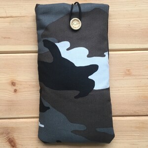 Pode incluir: Uma capa de telefone camuflada com uma al&ccedil;a el&aacute;stica preta e um bot&atilde;o de madeira que diz "Handmade with love".