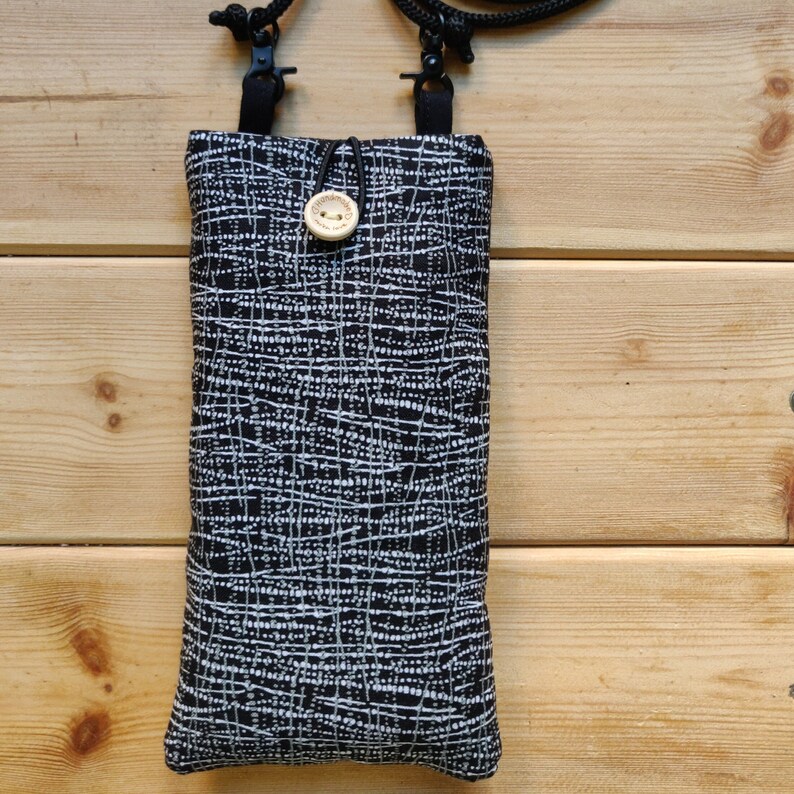 Pode incluir: Uma bolsa de telefone com padr&atilde;o preto e branco com uma al&ccedil;a preta e um fecho de bot&atilde;o de madeira.