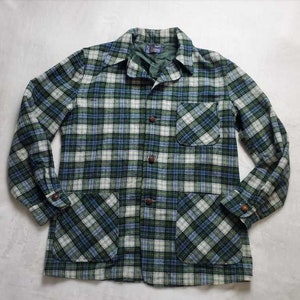 Può includere: Giacca a quadri verdi, blu e bianchi con due tasche frontali e bottoni marroni. La giacca ha un colletto e maniche lunghe. Il motivo a quadri è un design classico, adatto all'abbigliamento casual.