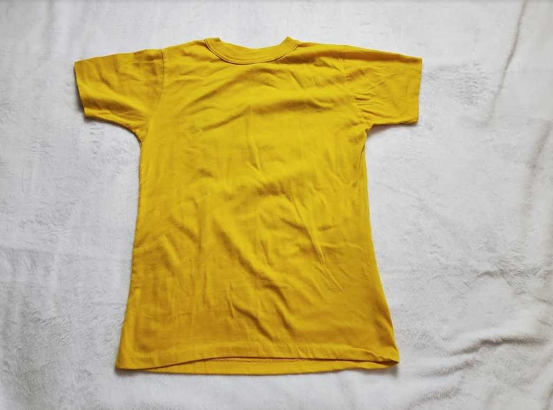 May include: A solid yellow t-shirt with a crew neck and short sleeves. The shirt is made of a soft fabric and is laid flat on a white surface. The t-shirt is a basic, casual garment.