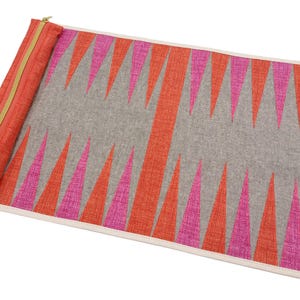 May include: A pink and orange patterned backgammon board with a zippered carrying case. The board is made of a soft, textured fabric and folds up for easy storage.