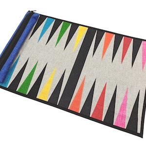 May include: A backgammon board featuring a grey playing surface and black edges. The triangles are in a variety of colours, including green, yellow, orange, and pink. A blue and black zipped pouch is attached.