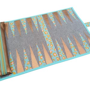 Op de afbeelding: Een turquoise blauwe en gouden backgammonset met een luipaardprint. De set vouwt samen tot een compacte draagtas.