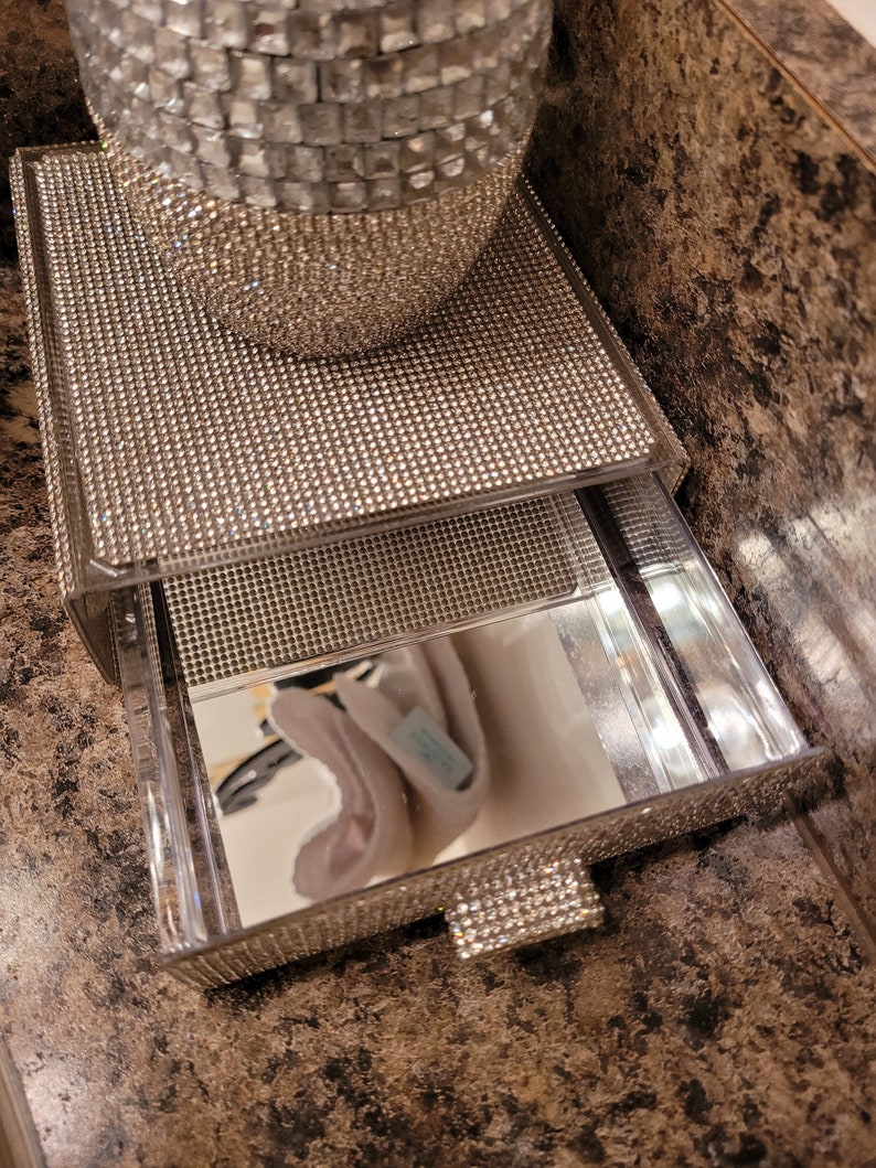 May include: A two-tiered mirrored tray with a clear acrylic drawer. The tray is covered in rhinestones and has a mirrored surface. The drawer is also covered in rhinestones and has a clear acrylic handle.