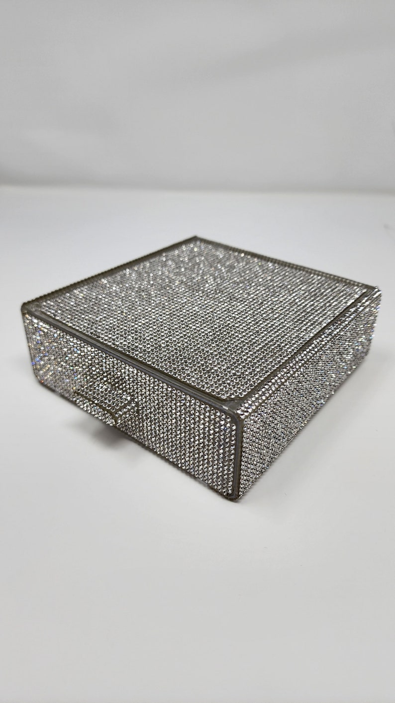 May include: A small, square-shaped box covered in sparkling rhinestones. The box has a small drawer on the front.