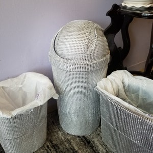 May include: Three silver trash cans with a diamond-like pattern. The trash cans are lined with white trash bags.