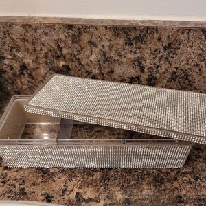 May include: A clear plastic rectangular box with a lid covered in rhinestones. The box has multiple compartments.