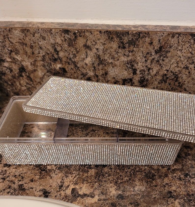 May include: A clear plastic rectangular box with a lid covered in rhinestones. The box has multiple compartments.