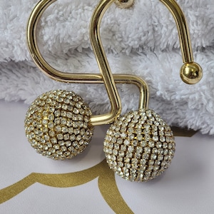 May include: Two gold shower curtain hooks with clear rhinestone embellishments.