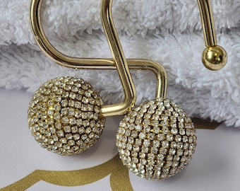 May include: Two gold shower curtain hooks with clear rhinestone embellishments.