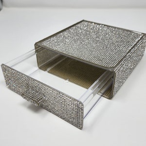 May include: A clear plastic drawer box with a pull-out drawer. The box and drawer are covered in silver rhinestones.