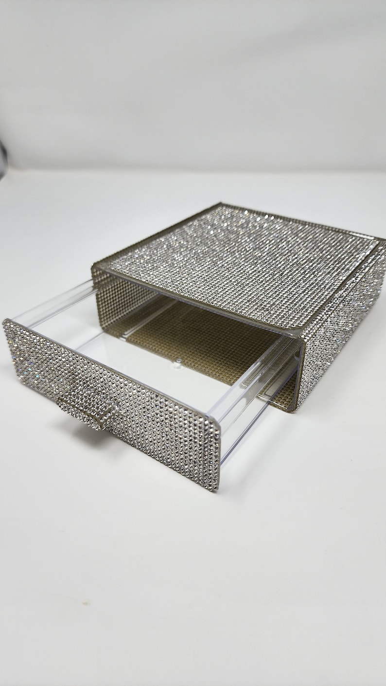 May include: A clear plastic drawer box with a pull-out drawer. The box and drawer are covered in silver rhinestones.