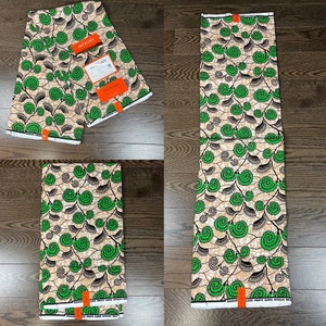 May include: Green and brown African wax print fabric with a swirling pattern. The fabric is folded in half and has a label that says "Super African Wax" on it.