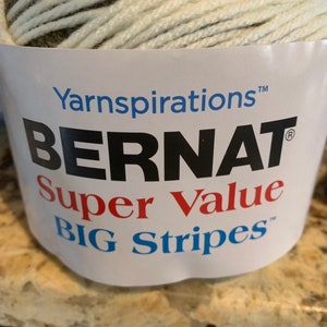 May include: A skein of Bernat Super Value Big Stripes yarn in a green, white, and brown color combination. The yarn is labeled with the Bernat brand name and the yarn weight.