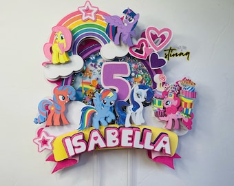May include: A colorful cake topper featuring My Little Pony characters, a rainbow, a number 5, and the name "Isabella".