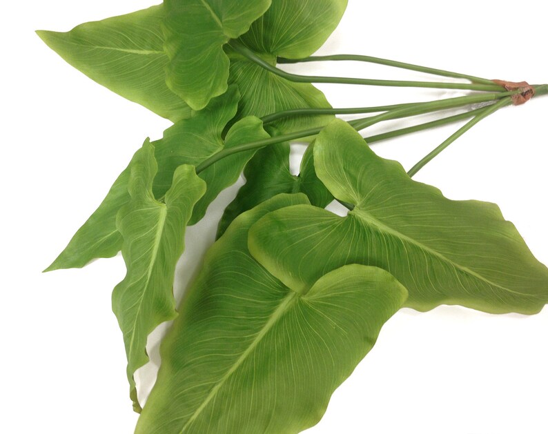May include: A cluster of artificial green leaves with prominent veining. The leaves are heart-shaped and arranged on slender green stems, bound together with a brown tie. The background is plain white.