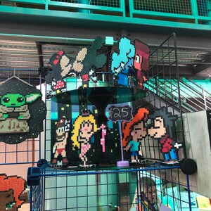 May include: A display of pixel art characters, including Mickey and Minnie Mouse, and characters from video games and cartoons. The art is displayed on a black wire grid shelf. The price tag reads $25.