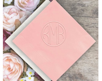 May include: Pink paper napkins with a white embossed circle containing the monogram "RMB" in a modern font.